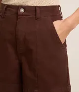 Short regular de talle alto confeccionado en sarga de color marrón, con trabillas para cinturón, cierre con botón y cremallera, bolsillos delanteros y traseros, y pespuntes en contraste.