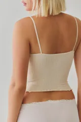 Top corto sin costuras de tejido acanalado y texturado color marfil, con escote redondo amplio, botonadura henley al frente con pequeños botones a presión, tiras finas fijas y terminación con ruedo en lechuga, de calce ajustado.