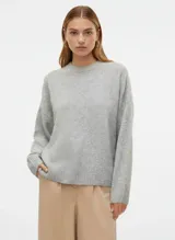 Suéter de punto grueso (chunky) color gris claro melange, con cuello redondo y hombros caídos. Presenta puños y bajo acanalados.