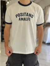 Remera de algodón pesado de corte oversize en color blanco, con cuello redondo y ribetes en las mangas de color azul marino. Cuenta con un estampado frontal con el texto "POSITANO AMALFI".