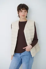 Chaleco acolchado tipo puffer, color beige, sin mangas, con cuello redondo y cierre frontal con botones a presión.