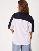 Remera oversize de manga corta marca Rusty, modelo Rocca, en combinación de colores celeste, blanco y detalles en verde. Presenta estampado frontal con el logo de la marca y diseño de bloques de color.