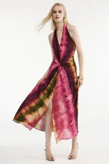 Vestido midi de cuello halter y escote en V, con diseño tie-dye en tonos fucsia, borgoña y verde. Presenta un nudo decorativo en el delantero, espalda descubierta y abertura frontal en el bajo.