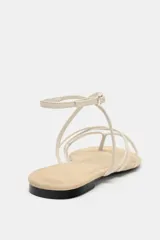 Sandalia plana de diseño minimalista con múltiples tiras finas en el empeine y cierre de pulsera con hebilla metálica en el tobillo.