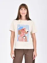 Remera de algodón color beige con estampa frontal de un perro con boina, anteojos y una taza de café sobre un fondo de rayas verticales azules.