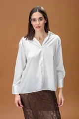 Camisa blanca de corte clásico y diseño holgado, con cuello camisero, cierre frontal de botones y mangas largas con puños anchos.