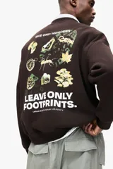 Buzo de cuello redondo en color marrón oscuro, con diseño de hombros caídos y estampado pequeño en el pecho con la frase 'Leave Only Footprints'. Presenta puños y bajo acanalados.