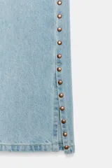 Jeans de tiro medio con cinco bolsillos, pernera recta y diseño de tachas laterales con bajo con abertura. Cuenta con cierre frontal con cremallera y botón.