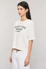 Remera Kosiuko de algodón color blanco, de corte regular y mangas cortas hasta el codo. Cuenta con un diseño estampado en el frente con la leyenda "Messy Chic Kosiuko St. Tropez".