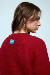 Cardigan corto de punto color rojo, con cierre frontal y cuello redondo. Presenta una textura acanalada y mangas largas.