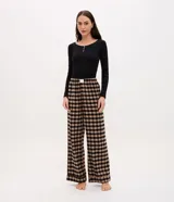 Pantalón de pijama de corte holgado confeccionado en franela con estampado de cuadros en tonos beige y negro. Presenta cintura elástica con botones decorativos en la parte frontal.