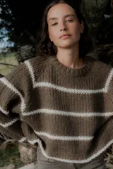 Buzo de tejido de punto grueso en color gris con rayas horizontales en color crema, de corte holgado, cuello redondo y mangas largas.