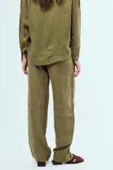 Pantalón largo negro de corte holgado y tiro medio, con costuras visibles en color blanco que delinean su diseño y bolsillos.