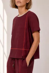 Blusa de lino color beige, de manga corta y cuello redondo, con detalles de costuras decorativas verticales y una línea horizontal bordada en tono contrastante.
