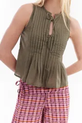Blusa blanca sin mangas de algodón, con diseño de tablas frontales y escote con lazos para atar.