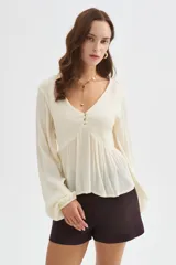 Blusa de viscosa color blanco marfil, con escote en V, detalles de frunces en el frente, botones decorativos y mangas largas abullonadas con puños elásticos.