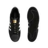 Championes Adidas modelo Superstar ADV, de diseño clásico con exterior de cuero negro, las icónicas tres tiras laterales en blanco y la característica puntera de goma. Incluye el logo Superstar en dorado en el lateral y el logo de la marca en la lengüeta y el talón.