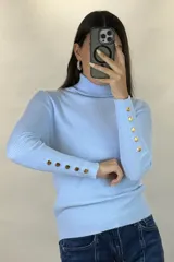 Polera de hilo blanca de cuello alto y manga larga, con detalle de botones dorados en los puños. Tejido de punto acanalado ajustado al cuerpo.