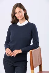 Buzo tejido en hilo de algodón color beige, con cuello redondo y manga larga. Presenta un corte clásico y un pequeño detalle metálico en la parte inferior izquierda.