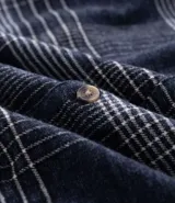 Camisa de manga larga confeccionada en franela de algodón, con cuello bowling y cierre frontal de botones. Presenta un diseño de estampado a cuadros en tonos azul marino y gris, con un corte regular.