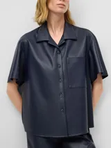Camisa de manga corta confeccionada en cuero sintético color azul marino. Presenta un diseño de línea recta, cuello solapa, cierre frontal con botones y un bolsillo aplicado en el pecho.