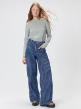 Pantalón de tiro medio y pierna ancha confeccionado en denim de algodón grueso. Presenta un diseño a rayas verticales en tonos azul y celeste, con costuras en contraste color rojo, bolsillos laterales tipo cargo y remaches metálicos.