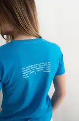 Remera de algodón blanca, con cuello redondo y mangas cortas. Presenta un estampado frontal con la palabra "KAPSUL" en rojo sobre un diseño floral en tono beige.
