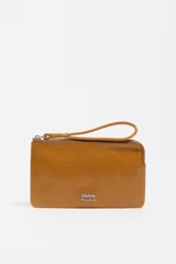 Monedero de cuero vacuno color tostado con cierre superior y correa de muñeca integrada. Presenta el logo metálico de la marca en la parte frontal.