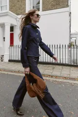 Camisa entallada de denim azul oscuro con cuello solapa, manga larga y cierre frontal con botones metálicos. Presenta un bolsillo de plastrón en el pecho y costuras a contratono.