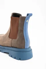 Bota tipo Chelsea de cuero lavado en tono marrón, con paneles laterales elásticos en color marrón oscuro. Presenta una suela track robusta de goma en color azul y un tirador trasero en el mismo tono azul.
