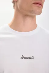 Remera blanca de manga corta con cuello redondo y estampado trasero en tono sepia/marrón. El estampado incluye el texto "Aloha Hawaii" y una ilustración de una caseta de salvavidas con el texto "Paradise of the Pacific".