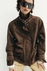 Chaqueta de tejido efecto ante color marrón, con cuello alto, cierre frontal con cremallera y botones a presión, manga larga y bolsillos de plastrón con solapa en el delantero.