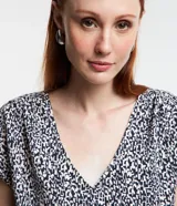 Blusa de crepé estampada en blanco y negro, con escote en V, mangas cortas y detalle de botones en los hombros.