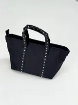 Bolso negro tipo tote bag con apliques de tachas plateadas en las asas y en los laterales.