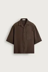 Camisa marrón de corte boxy fit, con tejido estructurado, cuello bowling, manga corta y un bolsillo aplicado en el pecho. Cuenta con cierre frontal de botones.