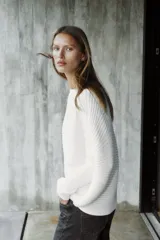 Sweater de punto blanco con textura acanalada horizontal, cuello barco, mangas largas amplias y corte holgado.