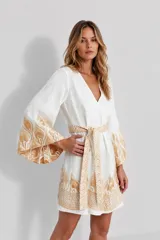 Minivestido blanco de lino con escote en V, mangas anchas acampanadas y bordados dorados en los puños, el dobladillo y el cinturón ajustable.