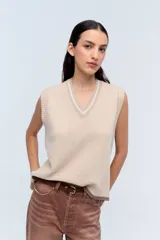 Chaleco de punto color beige con escote en V y ribete blanco.