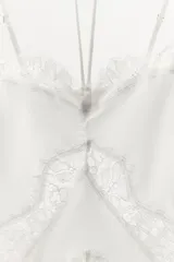 Body confeccionado en mezcla de seda con escote en pico y tiras ajustables al cuello con lazada. Presenta tirantes finos regulables y aplicaciones de encaje a tono en el frente y los bordes. Cuenta con cierre de ganchos en la espalda y botones a presión en el bajo.