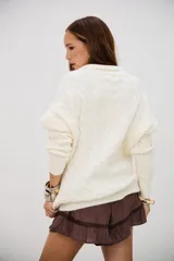 Sweater de punto grueso color crudo, con cuello polo y escote en V. Presenta un diseño de trenzas en toda la prenda y es de corte holgado.