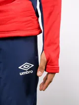 Buzo de entrenamiento Umbro del Club Nacional de Football, con cierre frontal parcial y cuello alto. Presenta un diseño con bloques de color azul, blanco y rojo, con panel frontal acolchado y mangas largas con aberturas para pulgares.