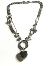 Collar de cadena de eslabones plateados con diseño asimétrico que incorpora un alfiler de gancho, esferas metálicas y un dije central en forma de corazón.