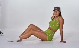 Conjunto deportivo compuesto por un top y un short de tiro alto en color verde oliva. El top presenta escote redondo y costuras decorativas en contraste, mientras que el short cuenta con un diseño ajustado con costuras visibles y logo estampado en el top.