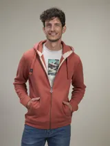 Buzo tipo hoodie con cierre frontal completo, capucha ajustable con cordones y bolsillos tipo canguro. Presenta un diseño de tejido de punto en color terracota con forro interior en contraste.