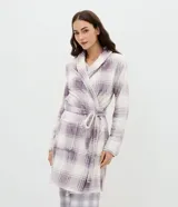 Bata de baño de corte regular confeccionada en tejido fleece suave y cálido. Presenta un diseño estampado a cuadros en tonos lila y blanco, con cuello solapa, cierre frontal mediante lazo ajustable a la cintura, mangas largas y bolsillos laterales.