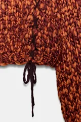 Jersey de punto grueso con textura trenzada en color naranja y bordó. Presenta cuello redondo, mangas largas abullonadas y detalle de cordones trenzados a contraste en el frente con terminación en lazada en el ruedo.