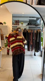 Sweater tejido de punto con diseño a rayas horizontales en tonos amarillo, celeste y marrón. Presenta un cuello polo con escote en V, mangas largas y un corte holgado.