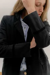 Tapado largo de jean azul oscuro, con cuello solapa y puños con detalle de cinta de terciopelo negro. Presenta costuras visibles que definen paneles y un logo bordado en la espalda.