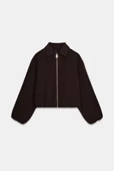 Chaqueta de corte corto y diseño abullonado en color marrón oscuro, con cuello solapa, mangas largas con puños elásticos y cierre frontal con cremallera metálica. Cuenta con bolsillos delanteros de doble vivo.