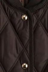 Campera de tejido guateado con diseño de rombos, cuello redondo acanalado, cierre frontal con botones a presión y bolsillos laterales. Presenta ribetes en los bordes y forro interior.
